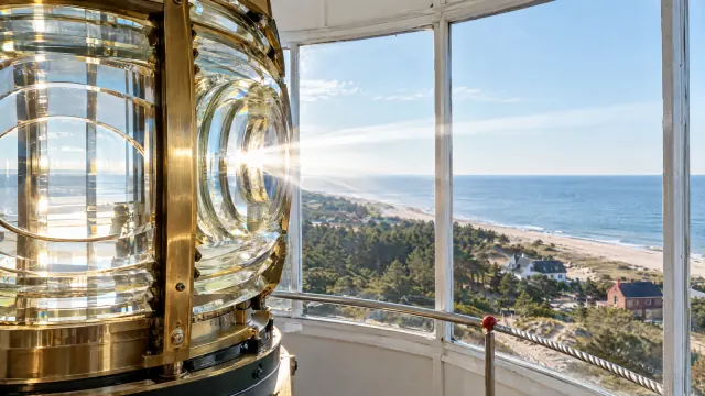 Messinggefasste Leuchtturmlinse im Laternenraum, durch die Fenster Kiefernwald, Dünen, Strand und Ostsee