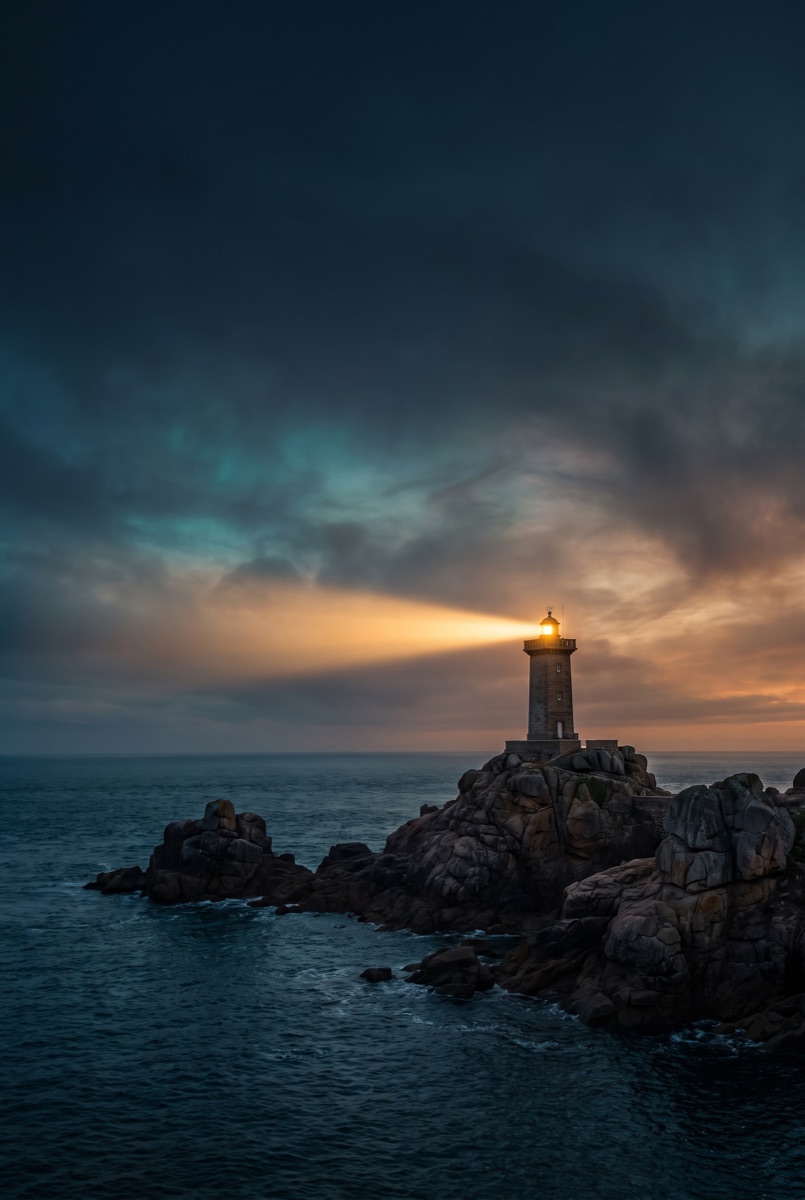 Leuchtturm mit Lichtstrahl an der Ostseeküste bei Dämmerung, Symbol für sichere Orientierung im Marketing